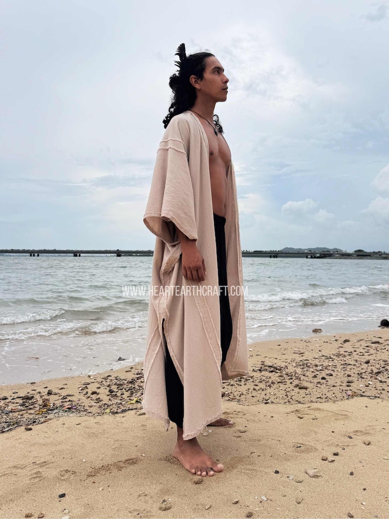 Pu&ograve; includere: Un abito a kimono beige con apertura frontale, maniche ampie e aspetto strutturato. L'abito &egrave; indossato sopra pantaloni neri. L'immagine include il testo "www.heartearthcraft.com" in basso. La persona &egrave; in piedi su una spiaggia sabbiosa.