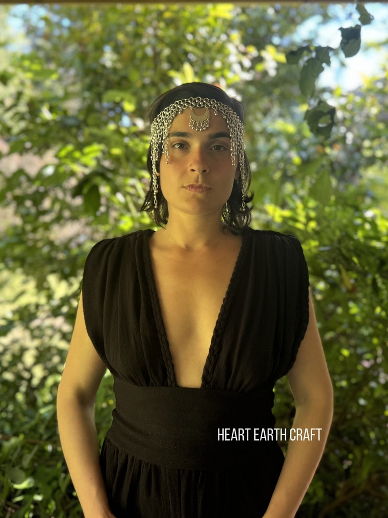 May include: A woman wearing a black sleeveless dress with a plunging neckline and a silver chain headpiece. The text "HEART EARTH CRAFT" is visible at the bottom of the image.