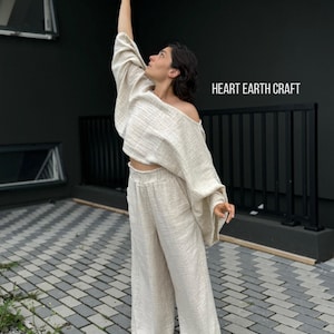 K&ouml;nnte beinhalten: Eine Frau tr&auml;gt ein locker sitzendes, cremefarbenes Leinenoberteil und eine passende weite Hose. Das Oberteil hat eine lockere, flie&szlig;ende Silhouette und die Hose einen bequemen elastischen Bund. Das Outfit ist ein schlichtes und elegantes Design, perfekt f&uuml;r warmes Wetter. HEART EARTH CRAFT steht in der oberen rechten Ecke des Bildes.