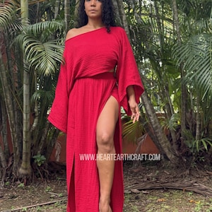 May include: A vibrant red two-piece set consisting of a loose-fitting, off-the-shoulder top with wide sleeves and a matching floor-length skirt featuring a high side slit. The fabric has a textured, crinkled appearance. Text reads HEARTEARTHCRAFT.COM.