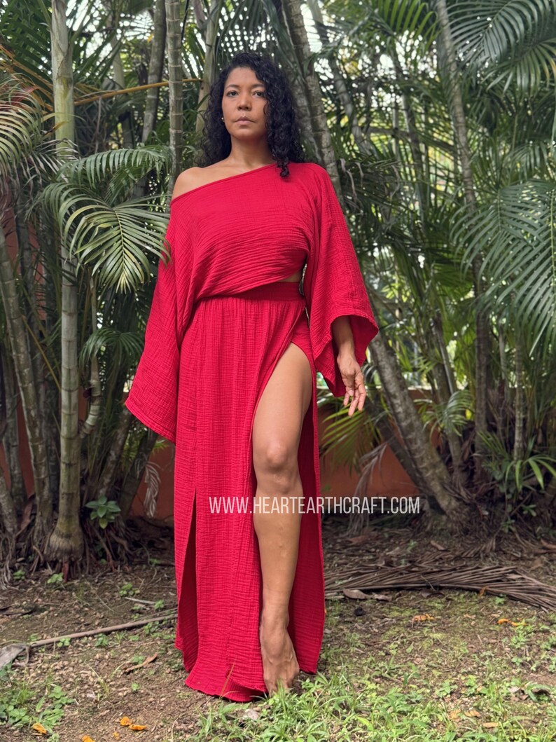 May include: A vibrant red two-piece set consisting of a loose-fitting, off-the-shoulder top with wide sleeves and a matching floor-length skirt featuring a high side slit. The fabric has a textured, crinkled appearance. Text reads HEARTEARTHCRAFT.COM.