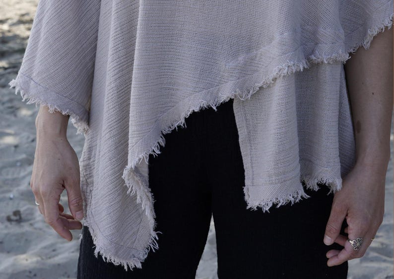 May include: A light gray, loose-fitting,  cotton top with a frayed hem. The top is draped over one shoulder and has a relaxed, casual style.