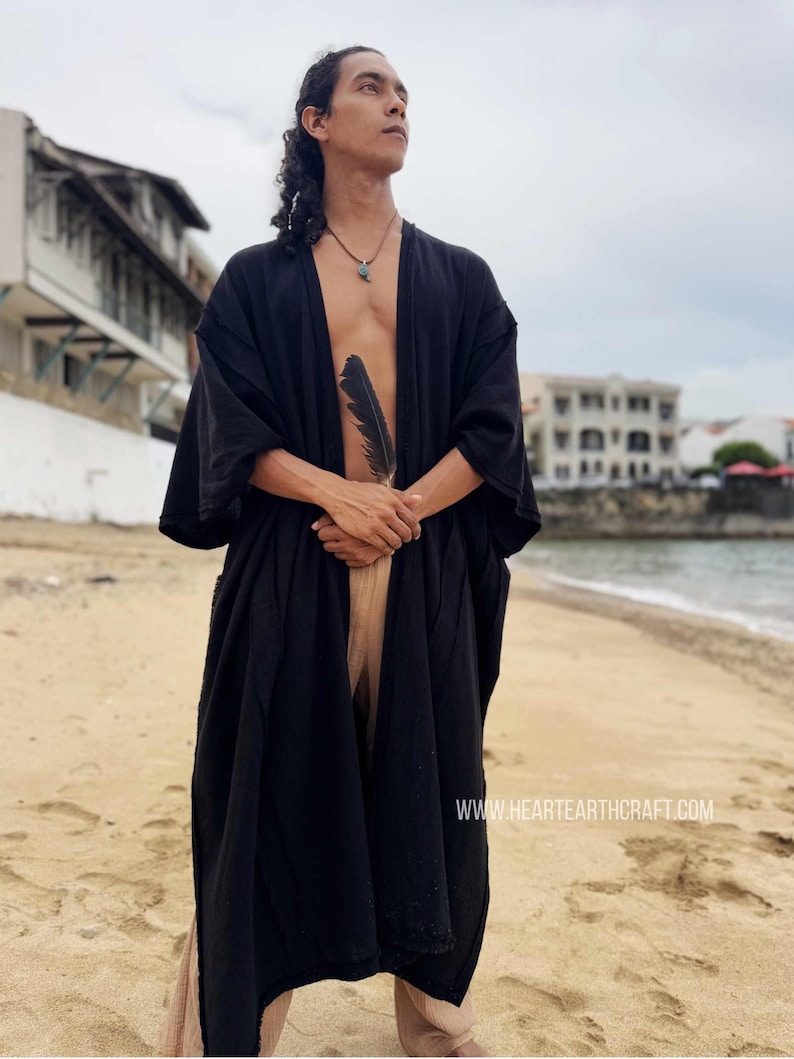 Pu&ograve; includere: Un kimono nero con maniche larghe. La veste &egrave; aperta sul davanti, rivelando uno scorcio del petto della persona e pantaloni beige. Una piuma nera &egrave; tenuta tra le mani. Lo sfondo &egrave; una spiaggia con edifici e il mare.