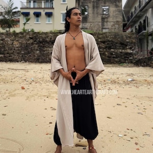 Pu&ograve; includere: Un completo beige e nero, composto da un lungo abito aperto e pantaloni a gamba larga, &egrave; indossato su una spiaggia. L'abito &egrave; beige da un lato e nero dall'altro. Il sito web www.heartearthcraft.com &egrave; visibile.