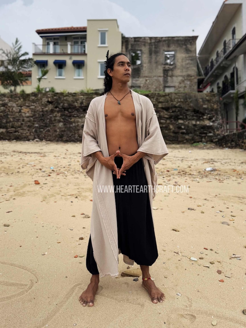 Pu&ograve; includere: Un completo beige e nero, composto da un lungo abito aperto e pantaloni a gamba larga, &egrave; indossato su una spiaggia. L'abito &egrave; beige da un lato e nero dall'altro. Il sito web www.heartearthcraft.com &egrave; visibile.