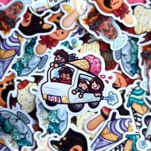 Puede incluir: Una pegatina con una furgoneta de helados blanca con figuras de dibujos animados dentro y encima. La furgoneta tiene el texto "FOB" en la parte delantera. Un gran cono de helado con chispas rosas está en la parte superior, rodeado de otras pegatinas coloridas.