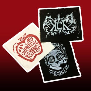 May include: Three square patches with white borders. One patch is off-white with a red apple design and the text "My Chemical Romance". Two patches are black with silver designs and text. One says "ICK" and the other says "Kill Joy Noise".
