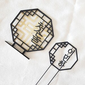 May include: Two black octagonal frames with Korean calligraphy inside. The larger frame has a gold background and the smaller frame has a white background.