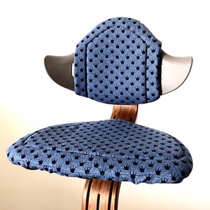 Könnte beinhalten: Ein blauer und grauer Stuhl mit einem Kronenmuster auf der Sitzfläche und der Rückenlehne. Der Stuhl hat ein Holzgestell.