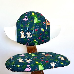 Könnte beinhalten: Ein blaugrünes Stuhlkissen mit einem Dschungeltier-Druck. Der Druck zeigt einen Flamingo, ein Krokodil, eine Giraffe, einen Tukan und zwei Tiger. Das Kissen ist gepolstert und hat eine weiße Rückseite.
