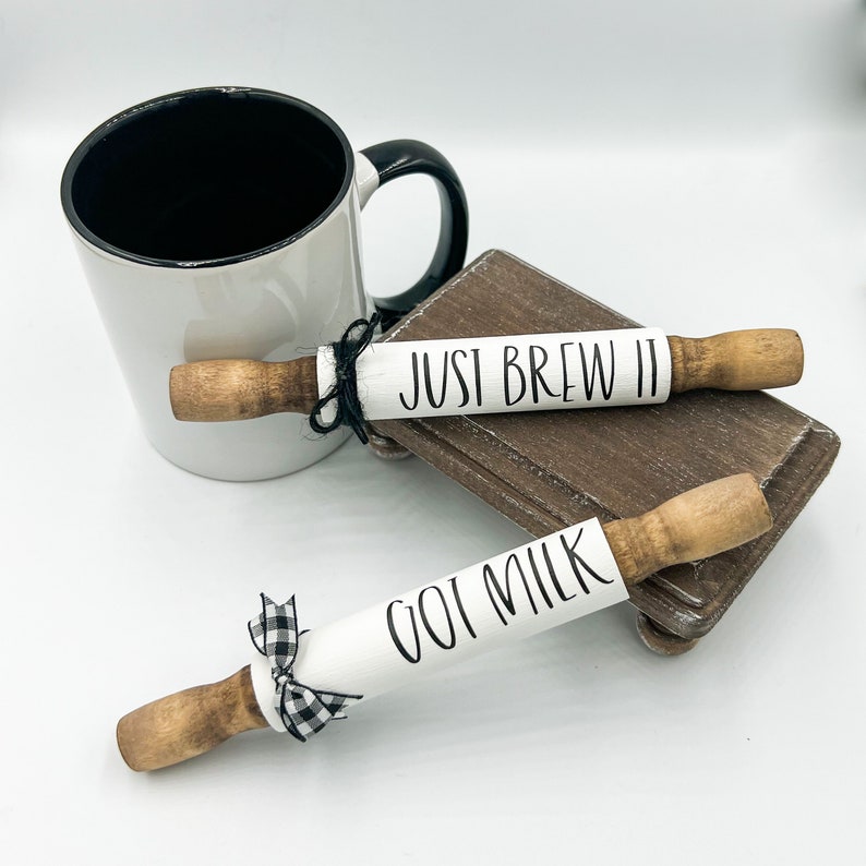 May include: Two white painted rolling pins with black lettering. One rolling pin says "JUST BREW IT" and the other says "GOT MILK". Both rolling pins have a black and white checkered ribbon tied around them.