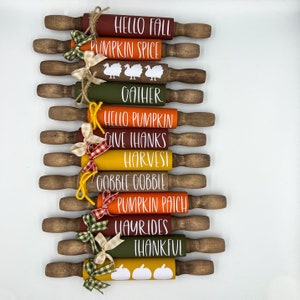 May include: A set of 10 wooden rolling pins decorated with fall-themed designs and text. The rolling pins are painted in various shades of orange, red, yellow, and green. The text on the rolling pins includes "Hello Fall", "Pumpkin Spice", "Gather", "Hello Pumpkin", "Give Thanks", "Harvest", "Gobble Gobble", "Pumpkin Patch", "Hayrides", and "Thankful".