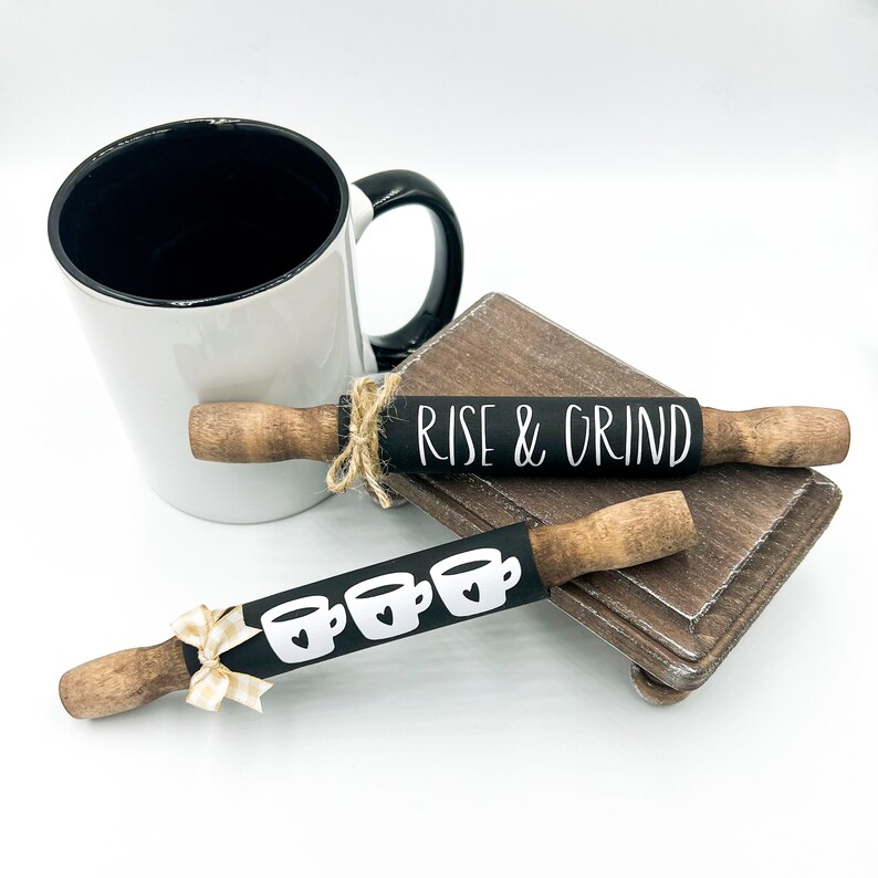 May include: Two black and white rolling pins with wooden handles. One rolling pin has the text "Rise & Grind" and the other has a row of four coffee cups with hearts.
