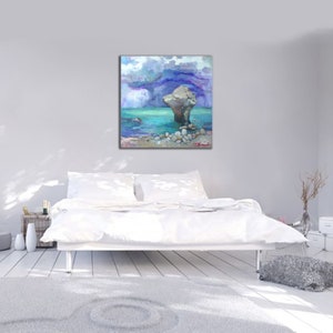 May include: Square canvas art featuring an abstract seascape painting. The artwork depicts a large rock formation in turquoise water under a stormy sky with shades of blue and purple. Small rocks are visible near the base of the rock formation.