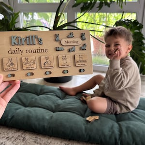 May include: A rectangular wooden daily routine board featuring the text Kirill's daily routine, with five square icons depicting tasks like Tidy Up Toys, Make Bed, Water Plants, Wash Face, and Play Music, plus sliding toggles below each icon.