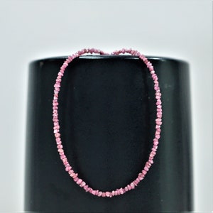 Op de afbeelding: Een roze diamanten ketting gemaakt van kleine, ruwe diamanten. De ketting ligt op een zwart oppervlak.
