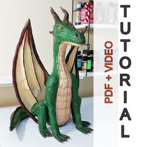 Könnte beinhalten: Ein grüner Papiermaché-Drache mit braunen und gelben Flügeln. Der Drache sitzt auf einer weißen Oberfläche. Das Bild enthält den Text "TUTORIAL PDF + VIDEO".