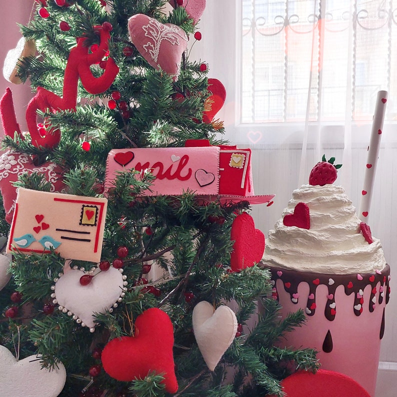 Pode incluir: Uma caixa de correio rosa e branca com a palavra "mail" nela, cercada por uma &aacute;rvore de Natal decorada com cora&ccedil;&otilde;es vermelhos e um milkshake rosa e branco com um morango no topo.