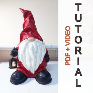 May include: A red and white paper mache gnome holding a small lantern. The gnome has a long white beard and a red hat. The gnome is standing on a white surface. The text "PDF + VIDEO TUTORIAL" is in the background.