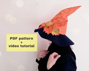 May include: A witch hat with a wide brim and a tall, pointed crown. The hat is made of felt and has a dark blue brim with an orange crown. The crown is decorated with orange and yellow felt leaves. The hat is being worn by a person, but the person's face is not visible. The text "PDF pattern + video tutorial" is visible in the image.