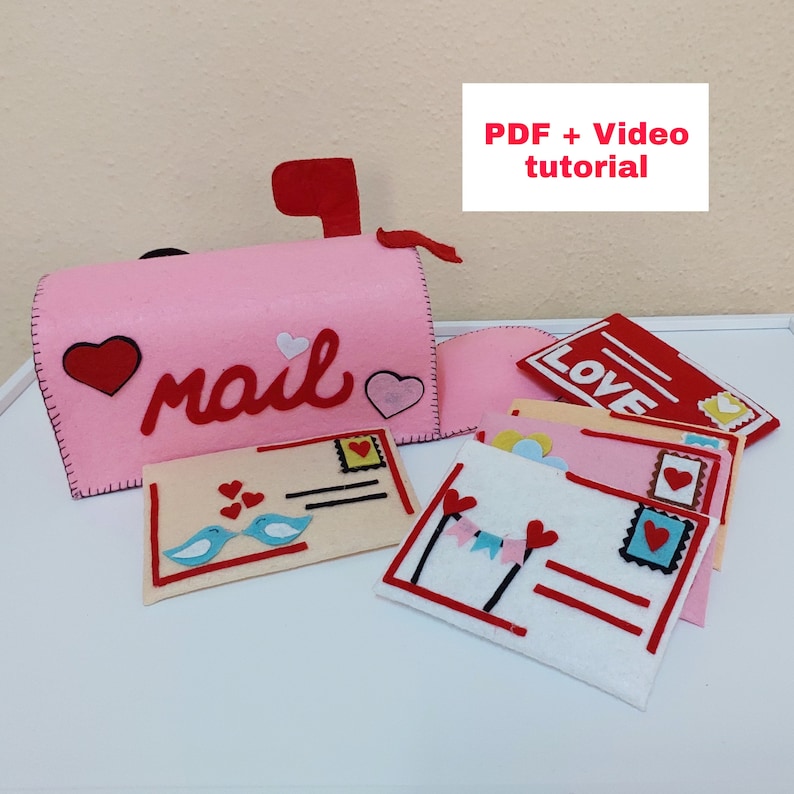 Pode incluir: Caixa de correio de feltro rosa com a palavra "mail" em letras de feltro vermelho. A caixa de correio tem uma aba de feltro vermelho e &eacute; decorada com cora&ccedil;&otilde;es de feltro vermelho. Existem v&aacute;rios envelopes de feltro com cora&ccedil;&otilde;es de feltro vermelho e outras decora&ccedil;&otilde;es. O texto "PDF + Video tutorial" est&aacute; no topo da imagem.