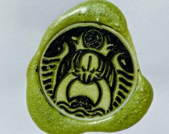 May include: A green wax seal with a black and white design of a creature with wings and a crown. The text "etsy: F2A99" is written below the seal.