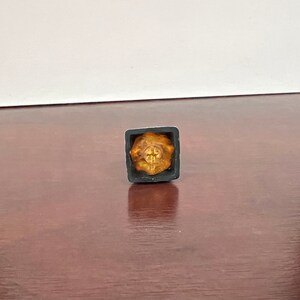 Op de afbeelding: Een gouden keycap met een kruisontwerp in een zwarte keycapbehuizing.