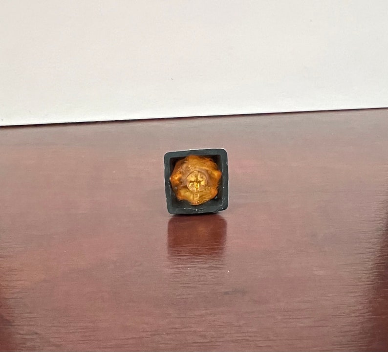 Op de afbeelding: Een gouden keycap met een kruisontwerp in een zwarte keycapbehuizing.