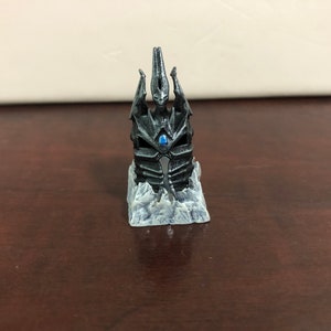 May include: A black and silver miniature replica of the Frostmourne, the Lich King's iconic sword, on a white icy base.