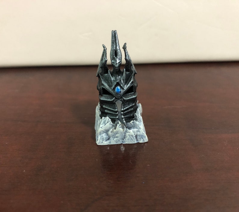 May include: A black and silver miniature replica of the Frostmourne, the Lich King's iconic sword, on a white icy base.