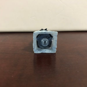 May include: A white and blue plastic keycap with a black key switch. The keycap has a textured surface and a square shape.