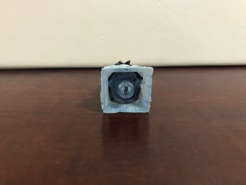 May include: A white and blue plastic keycap with a black key switch. The keycap has a textured surface and a square shape.