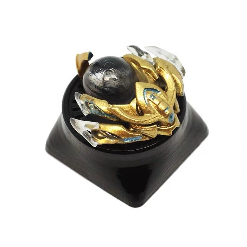 Puede incluir: Un tap&oacute;n de tecla dorado y plateado con un dise&ntilde;o detallado y una esfera negra en el centro. El tap&oacute;n de tecla est&aacute; montado sobre una base negra.