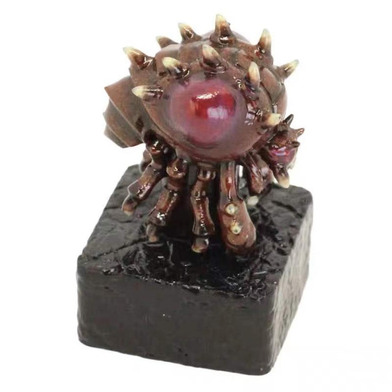 Puede incluir: Una peque&ntilde;a figura detallada de una criatura con un gran ojo rojo y muchas extremidades espinosas. La criatura est&aacute; de pie sobre una base negra texturizada.