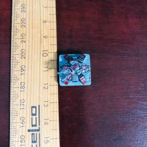 May include: A miniature grey and red robot with a gun, standing on a grey square base.