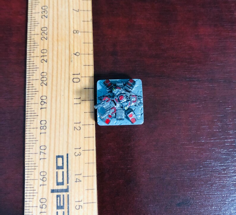 May include: A miniature grey and red robot with a gun, standing on a grey square base.