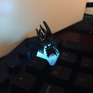 May include: A black 3D printed dragon claw keycap, glowing blue, on a black keyboard.
