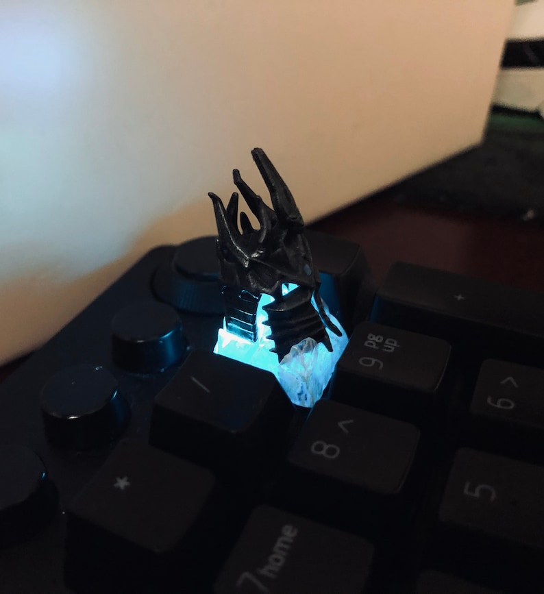 May include: A black 3D printed dragon claw keycap, glowing blue, on a black keyboard.