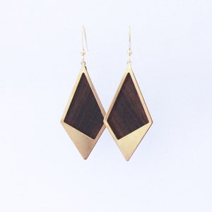Puede incluir: Un par de pendientes de tono dorado con una incrustación de madera oscura en forma de diamante.