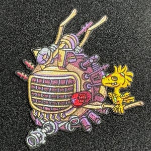 May include: Embroidered patch featuring a complex, multi-colored design. The patch includes a central, machine-like structure in shades of purple, yellow, and red, with a stylized yellow bird perched on a branch. The patch is on a dark gray background.