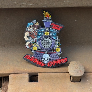 May include: An embroidered patch featuring a purple steam locomotive with a skull on the front, the number 666, and a figure in a blue cap. The text reads "IT RUNS ON BABIES" and "NIGHTMARE EXPRESS" in red lettering with flames at the top.