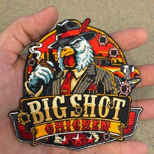 May include: An embroidered patch featuring a chicken dressed in a pinstripe suit, red tie, and fedora, holding a cigar. The text BIG SHOT CHICKEN is displayed in bold lettering above three red stars. The background includes a car and bullet holes.
