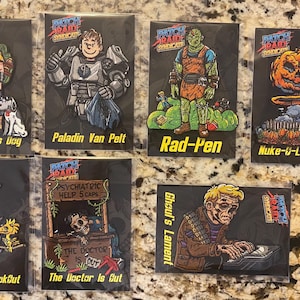 May include: Collection of seven rectangular patches with cartoon illustrations. The patches feature characters and text such as "A Boy & His Dog", "Paladin Van Pelt", "Rad-Pen", "Nuke-u-Lantern", "The Little Lookout", "The Doctor Is Out", and "Ghoul's Lament".