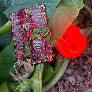 May include: A rectangular embroidered patch featuring a character in a red top hat and coat holding a glowing turnip. The character has long hair and a sinister expression. The patch is framed by an ornate border with flames at the bottom.