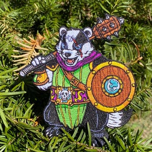 May include: Embroidered patch featuring a fierce badger warrior with a mace, shield, and sword. The badger is in black, white, and purple armor with a green and gold tunic. The shield is brown with a blue and white emblem.