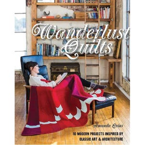 May include: A woman sits in a chair, wrapped in a red and pink quilt, reading a book. The book cover reads "Wanderlust Quilts" with the author's name and a subtitle about modern projects. A bookshelf and wooden ladder are in the background.