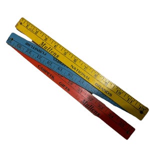 May include: Three vintage folding rulers in yellow, blue, and red. The yellow ruler has measurements up to 12 inches, the blue ruler up to 24 inches, and the red ruler up to 35 inches. Each ruler has text that reads "Mullens" and "Carpets, Gifts".