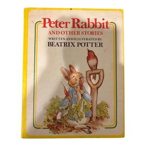 May include: A vintage hardcover book titled "Peter Rabbit and Other Stories" by Beatrix Potter. The cover features an illustration of Peter Rabbit holding a carrot, with a bird perched on a shovel. The book has a yellow border and a cream-colored background.
