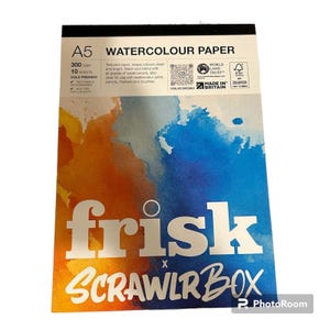 Puede incluir: Bloc de papel de acuarela A5 con el texto "WATERCOLOUR PAPER" y "frisk x SCRAWLR BOX". El papel es prensado en frío, 300 g/m², y contiene 10 hojas. El fondo presenta salpicaduras de acuarela naranja y azul.