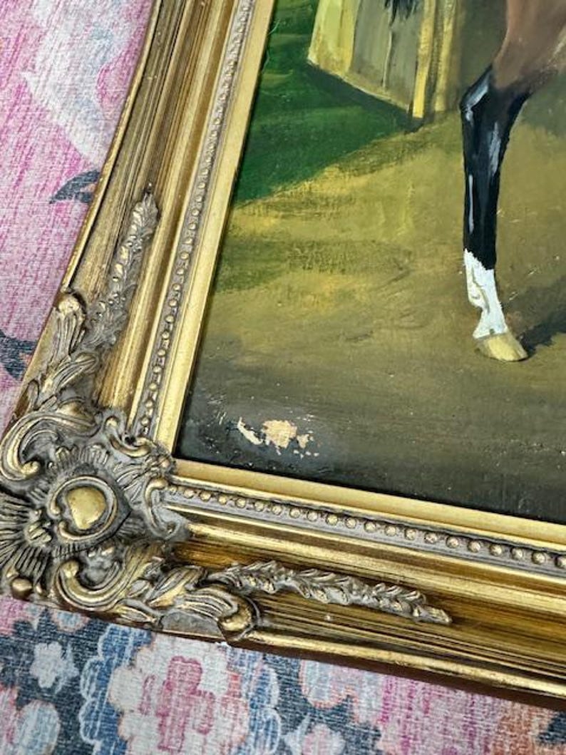 May include: An antique oil painting of a horse in a stable, framed in a gold ornate frame. The painting features a brown horse with black legs and a white marking on its leg. The frame has intricate details and a distressed finish.